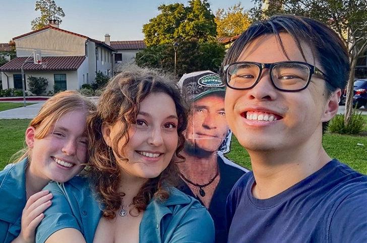 Students George Zhang, Annie Voss, and Annie Wion pose with a cardboard cutout of Survivor TV host Jeff Probst in the middle.