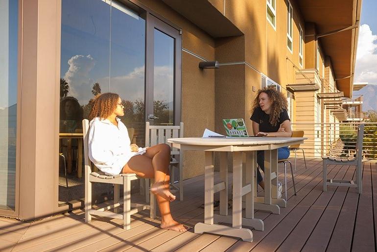 Two students sit at tables outside a dorm room